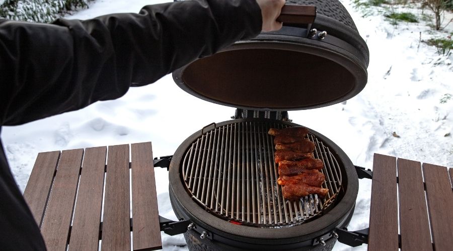 Meat on a grill with snow on the ground in the background.
