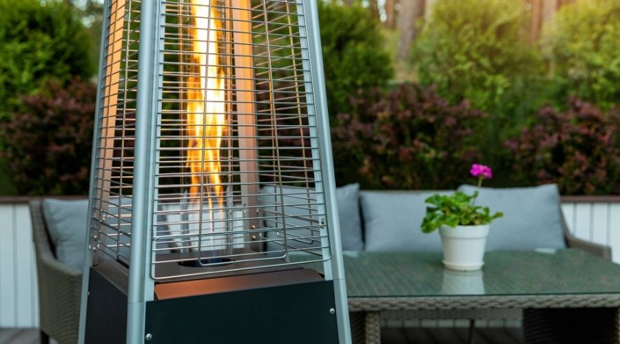 An outdoor heater on a backyard porch with outdoor furniture and plants in the background.