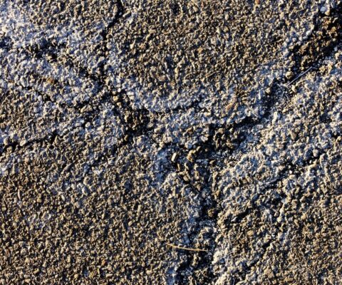 Unsealed asphalt showing signs of winter salt damage and cracks.