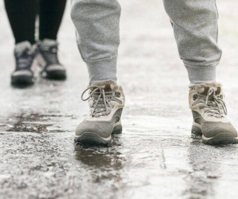 Close-up of the legs of two people who stand in snow boots on an icy sidewalk or driveway.